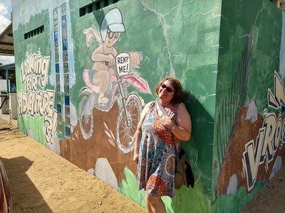 Jayne standing
        before a wall that is painted with the words Rent Me