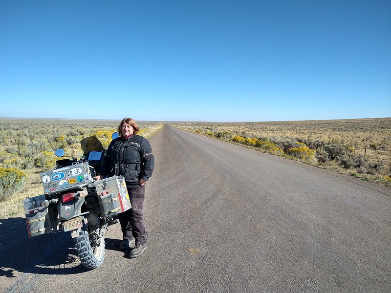 a woman stands next to her KLR motorcycle on a remote
        gravel road