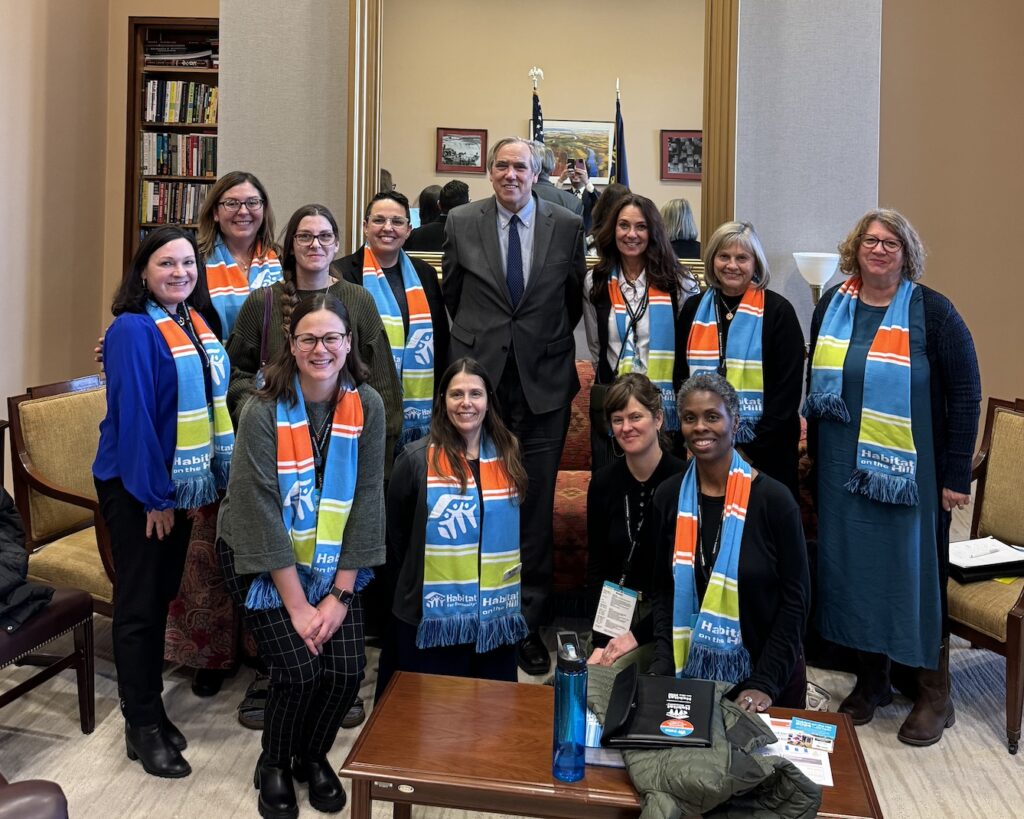 A group of women, all wearing matching, colorful scarves, pose with Senator Jeff Merkley (D-Oregon). 
